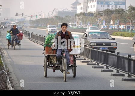 Chinese man riding a tricyle in a large street of Shanghai - China Stock Photo