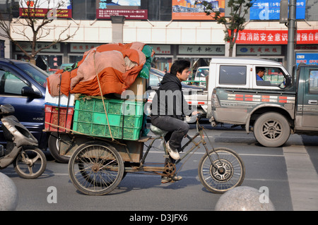 Chinese man riding a tricyle heavily loaded in a busy street of Shanghai - China Stock Photo