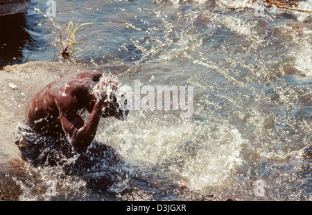Man sitting on a riverside rock, washing himself in the River Limpopo. Xai Xai. Mozambique Stock Photo
