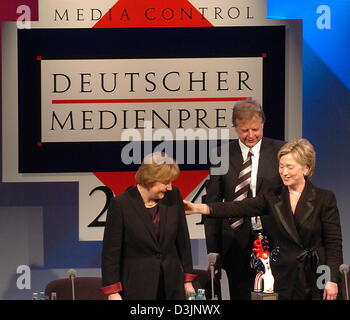 (dpa) - US Senator Hillary Clinton (R) smiles and reaches out to Angela Merkel (L), Chairwoman of the CDU, as she stands on stage with Merkel and Karlheinz Koegel, Head of Media Control and founder of the German Media Prize, in Baden-Baden, Germany, 13 February 2005.  Clinton was awarded the German Media Prize 2004 for her exemplary engagement advancing the role of women in the wor Stock Photo