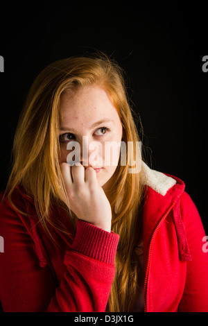 A shy nervous 16, 17 year old red haired freckle faced teenage girl, biting her finger nails UK Stock Photo
