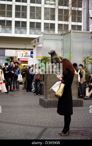 A young woman waiting in front of the Hachiko statue in Shibuya while texting, Tokyo, Japan Stock Photo