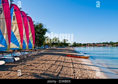 Line of catamaran sailboats with colorful sails early morning on Negril beach and kayak at the water Stock Photo