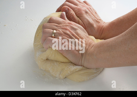 Two hands kneading bread dough on a white surface. Stock Photo