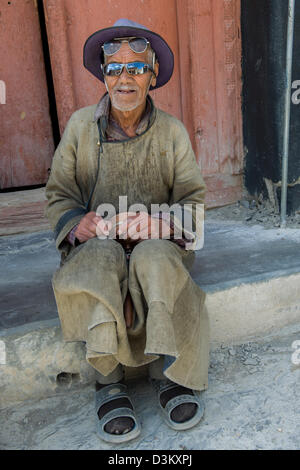 Elderly pilgrim wearing two pairs of sunglasses, sitting outside of Lamayuru Gompa, (Ladakh) Jammu & Kashmir, India Stock Photo