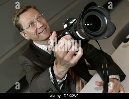 (dpa) - Guido Westerwelle, chairman of the FDP, holds the camera of a press photographer in his hands prior to a meeting of the FDP parliamentary faction in Berlin, Tuesday, 27 September 2005. The new faction had come together to elect the faction leader of the FDP to head the party at the German Bundestag. Current faction leader Gerhardt is expected to stay in office until May 200