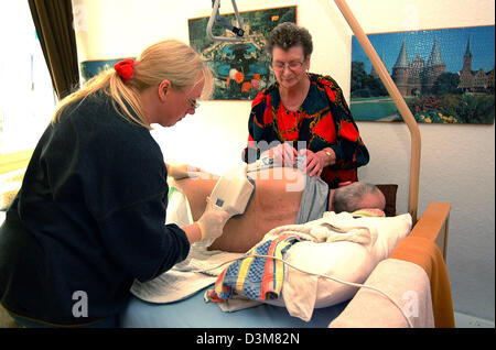 (dpa) FILE - A bedridden patient badly suffering from dementia and Parkinson's disease is given a massage by a nurse and his significant other (back), Hagen, Germany, 29 June 2004. Out-patient care of patients of care level III requires a high degree of dedication of nursing service staff member but also of the relatives. Photo: Klaus Rose Stock Photo