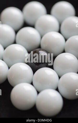 Contrasting white and black marbles used in game, one black pebble is left alone in opposition to all the white. Stock Photo
