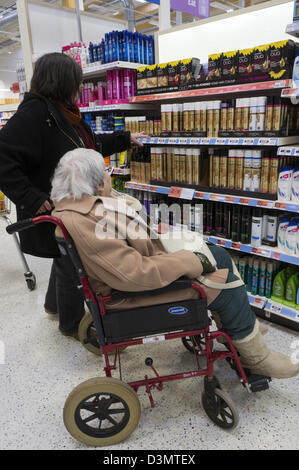 An elderly lady in a wheelchair and her carer or assistant look at hair products and shampoo in a supermarket. Stock Photo