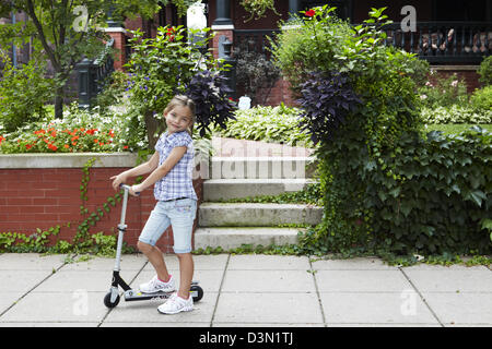 9 year old girl riding scooter on sidewalk Stock Photo