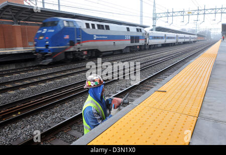 Railway worker works on a platform in Stamford, as an Amtrack Train passes behind him. CT USA Stock Photo