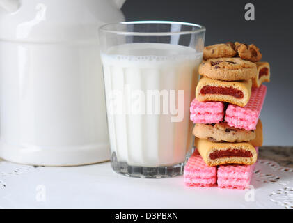 Closeup of a glass of milk with a stack of assorted cookies. Horizontal format on a light to dark gray background. Stock Photo