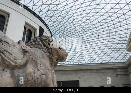 Lion in the Museum. A large weather worn stone lion presides over the covered courtyard of the British Museum. Stock Photo