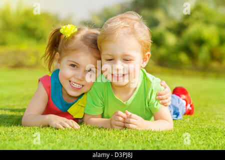 Image of two happy children having fun in the park, brother and sister lying down on green grass, best friends playing outdoors Stock Photo