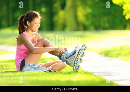 Mixed race Asian Chinese / Caucasian woman sitting in grass putting on inline skates at park Stock Photo