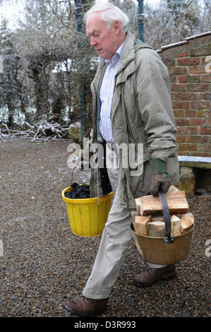 Pensioner carrying logs from log shed at home in north yorkshire uk Stock Photo