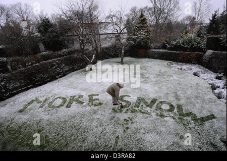 Elderly grandfather writing a humorous message MORE SNOW in snow in the garden Stock Photo