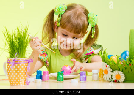 cute smiling child girl painting Easter eggs on green background Stock Photo