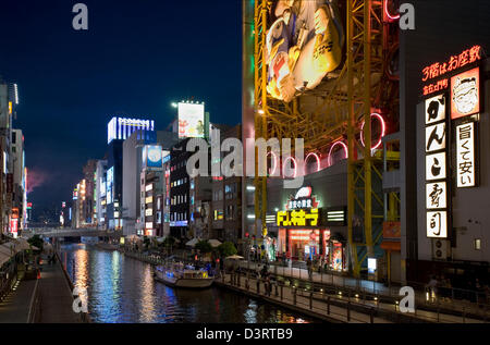 Sightseeing boat moves slowly past neon signs along Dotonbori-gawa (Dotonbori River) in Namba entertainment district of Osaka. Stock Photo