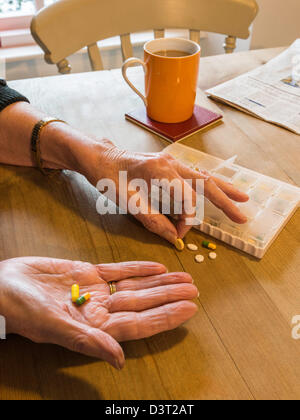 WOMAN AT TABLE WITH PILLBOX TAKING MEDICINE SORTING PILLS UK Stock Photo