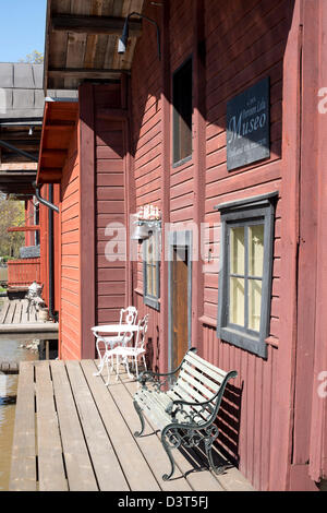 Bench, chairs and a small table on the terrace at the water in front of a traditional red wooden house in Porvoo, Finland Stock Photo