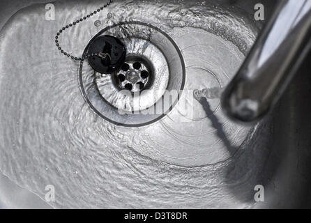 Tap water running down the plughole in a stainless steel kitchen sink Stock Photo