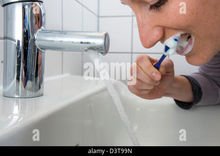 Woman is brushing her teeth, while water is still running from the tap. Symbol image for water wastage. Stock Photo