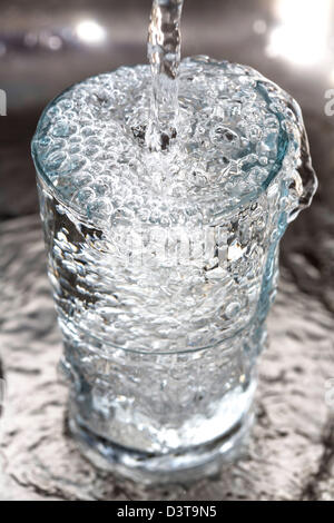 Water runs into a glass, from a tap in a kitchen. Stock Photo