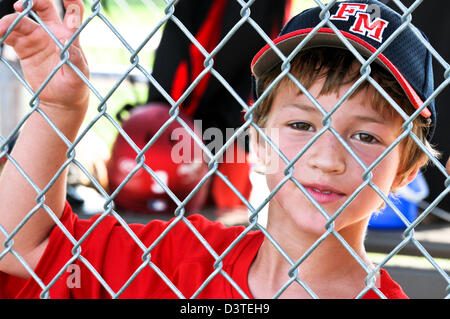 Up-close shot of a Little league baseball player standing in the dugout behind fence. Stock Photo