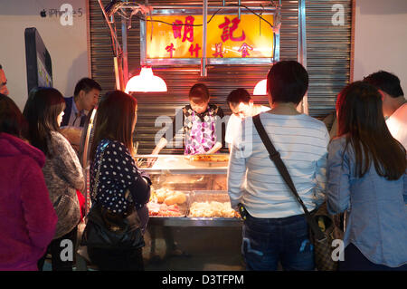 Street vendor selling fish balls and other delicacies in late night Macau, China SAR with a crowd gathered around Stock Photo