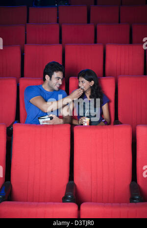 Couple enjoying popcorns while watching movie in a cinema hall Stock Photo