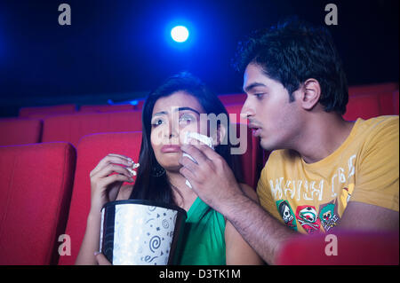 Man wiping tears of her emotional girlfriend while watching movie in a cinema hall Stock Photo