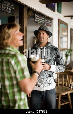 Two friends stand talking and drinking at bar, St Agnes, Cornwall, UK Stock Photo