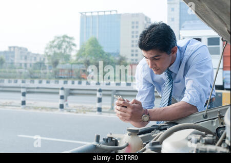 Businessman using a mobile phone near a broken down car, Gurgaon, Haryana, India Stock Photo