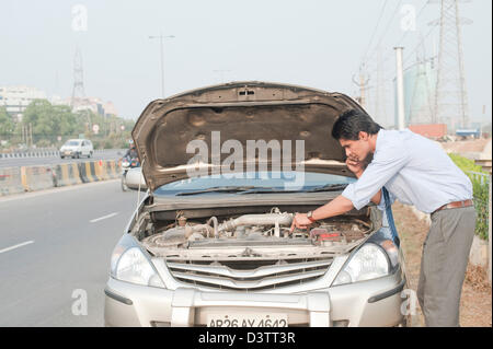 Businessman using a mobile phone near a broken down car, Gurgaon, Haryana, India Stock Photo