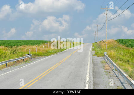 Country road heading over a hill under sunny blue skies with white clouds, a two lane summer highway in rural Pennsylvania, PA,