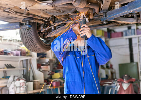 An auto mechanic works on chassis of car in his small business of car repair shop Stock Photo