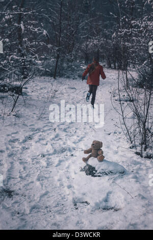 a teddy bear is sitting in the snow, a girl is running away Stock Photo