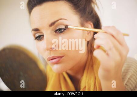 Attractive woman applying makeup while looking at the mirror Stock Photo