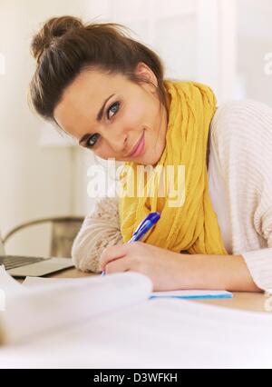 Closeup of a beautiful smiling woman looking at camera while writing on her notepad Stock Photo
