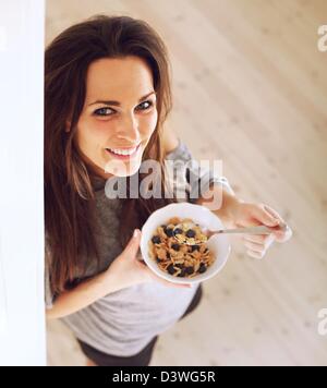 Cheerful lady holding a bowl of cereal while standing up and looking at you Stock Photo