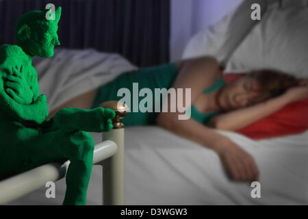 in the background a woman sleeps and in the foreground a little green devil, modelling clay, watches over her to ensure that she has bad dreams Stock Photo