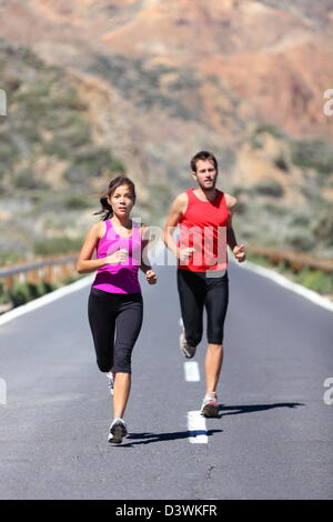 Full length of two runners training for marathon run outdoors on road in beautiful landscape Stock Photo