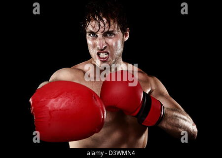 Strong muscular Caucasian man with boxing gloves hitting and punching looking angry isolated on black background Stock Photo