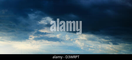Sunbeams in stormy dark cloudy blue sky. Panorama from several photos. Stock Photo