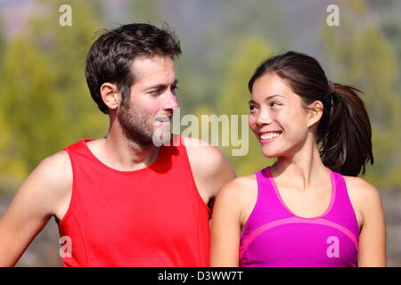 Happy Asian female athlete and Caucasian man smiling at each other while resting after running Stock Photo