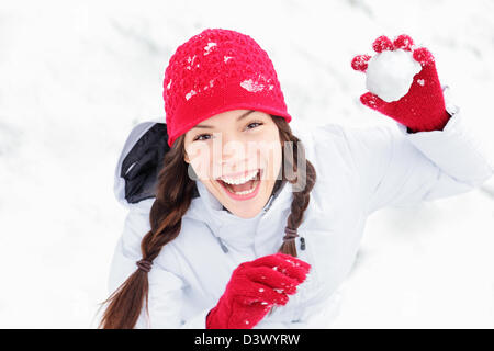 Cute playful multicultural Asian Caucasian young woman throwing snowball at camera having fun outdoors on snowing winter day Stock Photo