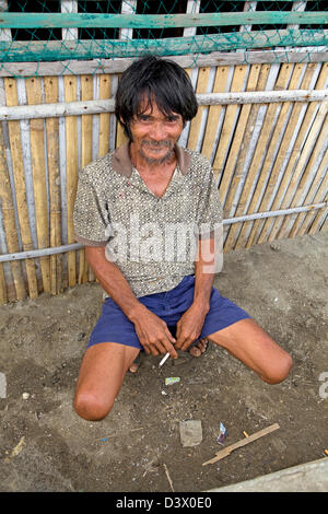 Portrait of a poor, Filipino man sitting by a fence smoking a cigarette. Stock Photo