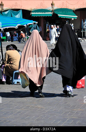 Two Moroccan women wearing the abaya or traditional dress for Arab women walking across the Jemaa El Fna plaza in Marrakech Stock Photo