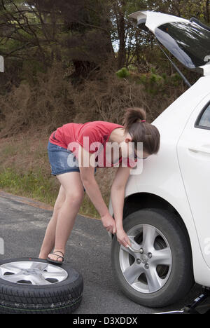 Young woman changes wheel at a remote roadside Stock Photo
